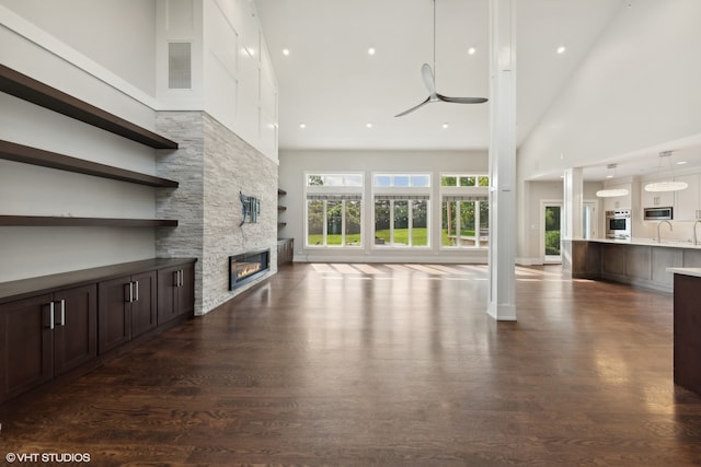 unfurnished living room with ceiling fan, a high ceiling, dark hardwood / wood-style flooring, and a stone fireplace