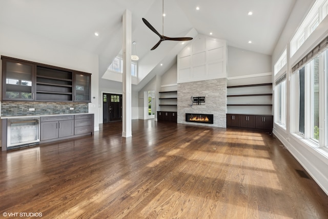 unfurnished living room with ceiling fan, a stone fireplace, dark wood-type flooring, and high vaulted ceiling