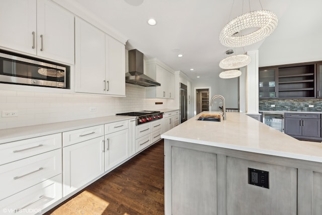 kitchen with wall chimney exhaust hood, beverage cooler, sink, white cabinetry, and built in appliances