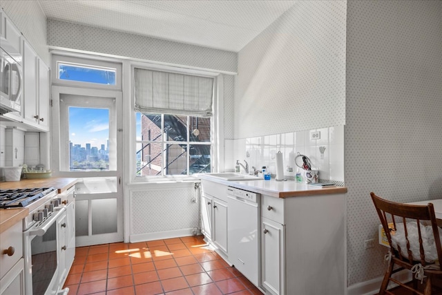 kitchen with white cabinetry, white appliances, backsplash, light tile patterned floors, and sink