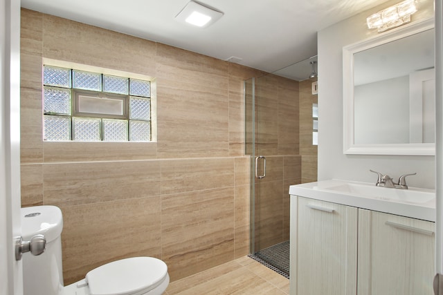 bathroom with a shower with door, vanity, tile walls, and toilet