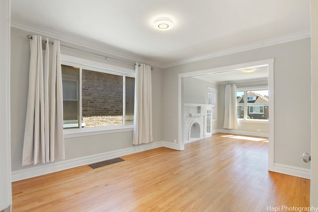 unfurnished living room with crown molding, light wood-type flooring, a brick fireplace, and a wealth of natural light