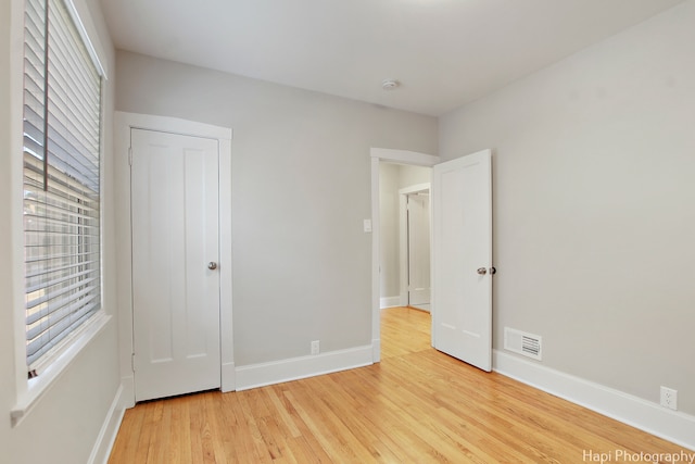 unfurnished bedroom featuring multiple windows, light hardwood / wood-style flooring, and a closet