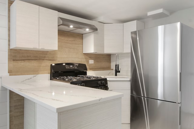 kitchen with wall chimney range hood, sink, light stone counters, stainless steel refrigerator, and gas stove