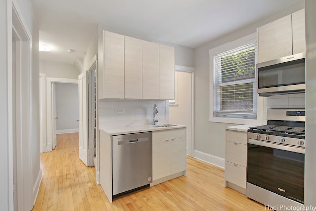 kitchen with light hardwood / wood-style flooring, light stone counters, stainless steel appliances, decorative backsplash, and sink