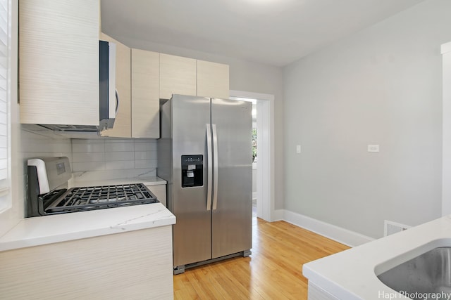 kitchen featuring light wood-type flooring, stainless steel refrigerator with ice dispenser, backsplash, stove, and sink