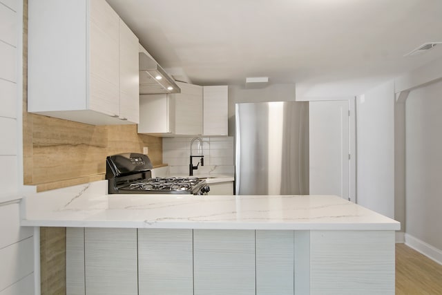 kitchen with light hardwood / wood-style flooring, black gas range, wall chimney range hood, kitchen peninsula, and light stone counters