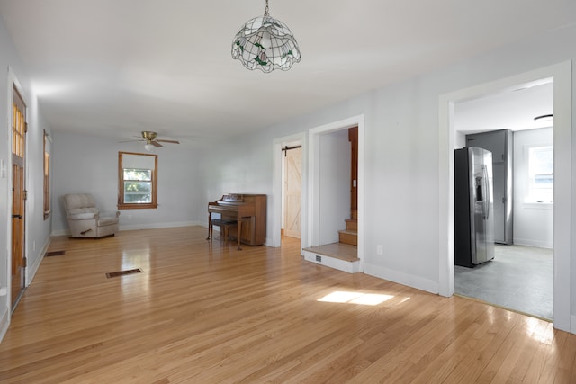 unfurnished living room with a barn door, light wood-type flooring, and ceiling fan with notable chandelier