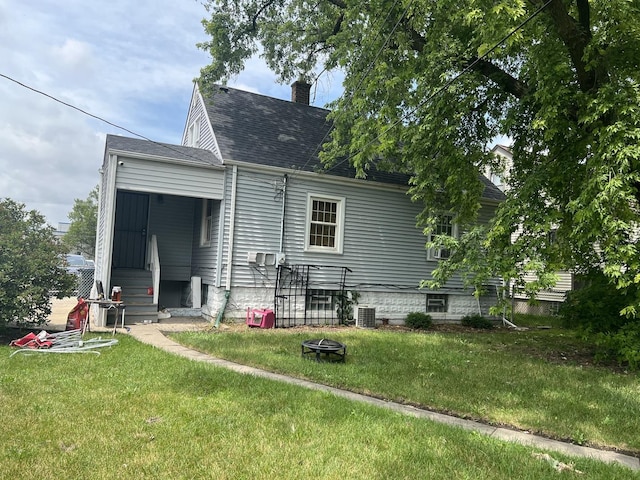 back of house with cooling unit, a lawn, and a fire pit