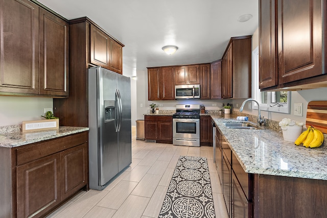 kitchen with appliances with stainless steel finishes, dark brown cabinetry, sink, and light stone counters