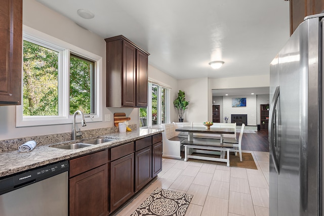 kitchen featuring sink, a brick fireplace, dark brown cabinets, appliances with stainless steel finishes, and light wood-type flooring