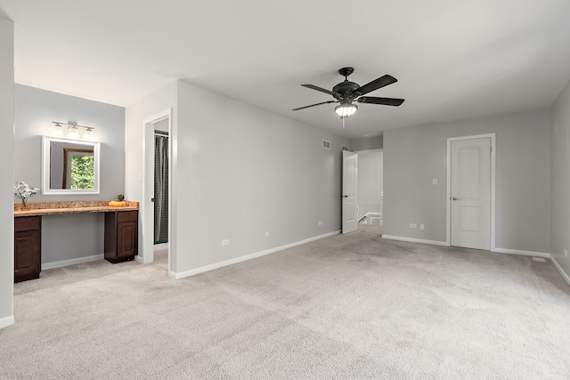 unfurnished bedroom with built in desk, ensuite bath, ceiling fan, and light colored carpet