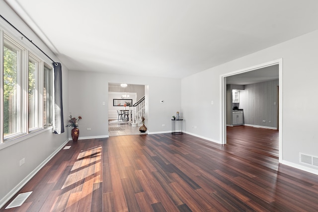 unfurnished living room featuring an inviting chandelier and dark hardwood / wood-style flooring