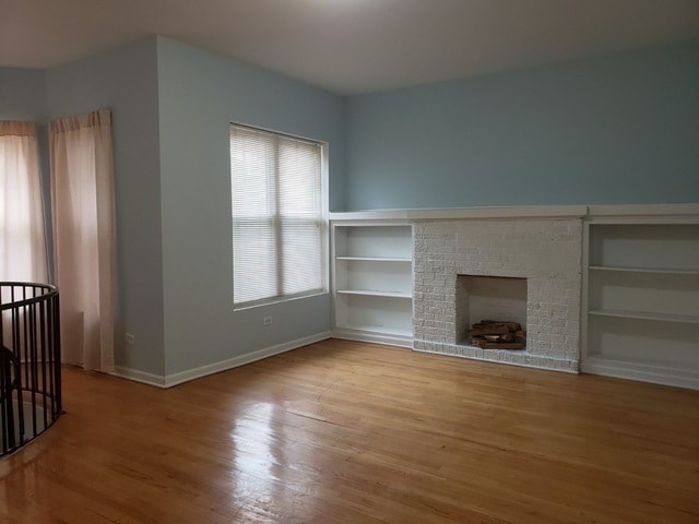 unfurnished living room with built in shelves, light hardwood / wood-style flooring, and a brick fireplace