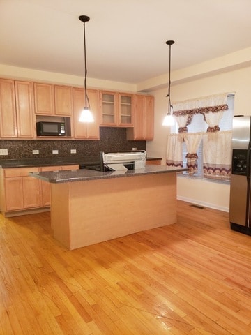 kitchen featuring stainless steel fridge with ice dispenser, light hardwood / wood-style floors, decorative light fixtures, and decorative backsplash