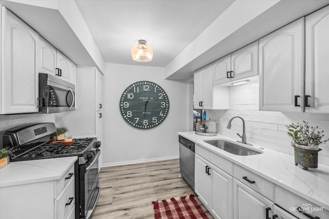 kitchen with white cabinets, light stone countertops, stainless steel appliances, light hardwood / wood-style floors, and sink