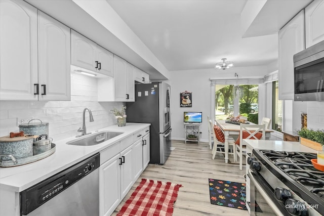 kitchen featuring appliances with stainless steel finishes, light hardwood / wood-style floors, white cabinetry, sink, and tasteful backsplash