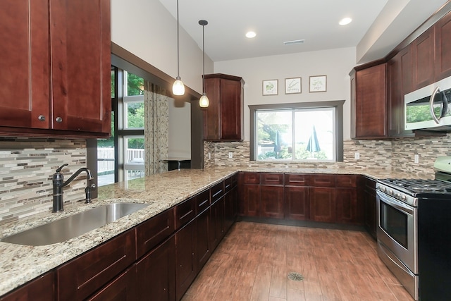 kitchen with sink, hanging light fixtures, light stone counters, kitchen peninsula, and stainless steel appliances