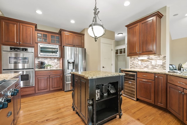 kitchen with a kitchen island, appliances with stainless steel finishes, wine cooler, light stone counters, and light wood-type flooring