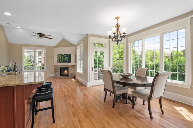 dining room with lofted ceiling, sink, a fireplace, ceiling fan with notable chandelier, and light wood-type flooring