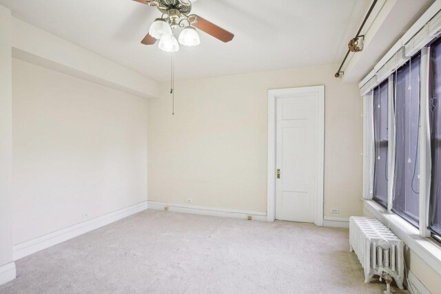 carpeted empty room with radiator and ceiling fan