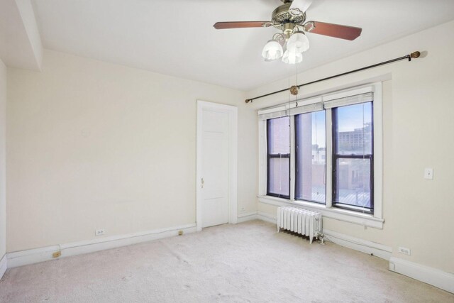 spare room featuring radiator heating unit, light colored carpet, and ceiling fan