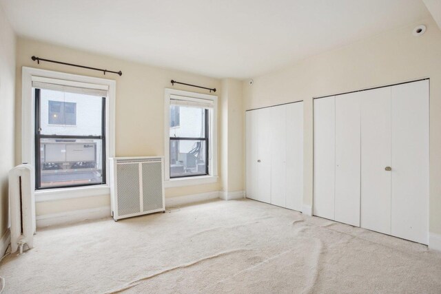 unfurnished bedroom with light carpet, radiator, and multiple closets