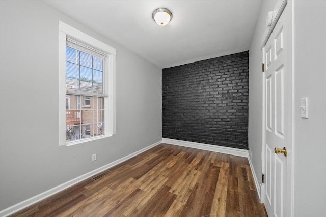 empty room with brick wall and dark wood-type flooring