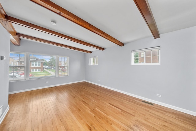 empty room featuring plenty of natural light, lofted ceiling with beams, and light hardwood / wood-style flooring