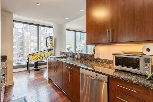 kitchen featuring stainless steel dishwasher, sink, dark stone counters, and dark hardwood / wood-style flooring