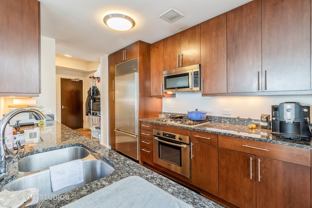 kitchen with sink, appliances with stainless steel finishes, and dark stone counters