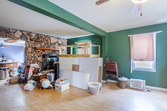 living room with a wall unit AC, a fireplace, ceiling fan, wood finished floors, and baseboards