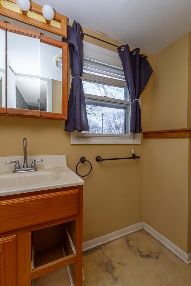 bathroom with unfinished concrete floors, baseboards, and vanity