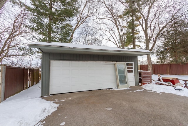 snow covered garage featuring fence and a detached garage