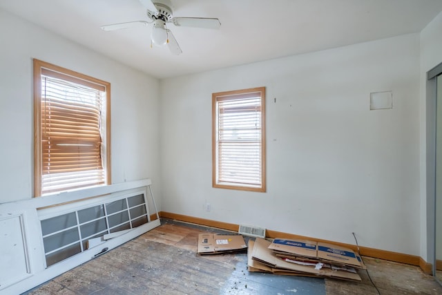 empty room with a ceiling fan, wood-type flooring, visible vents, and baseboards