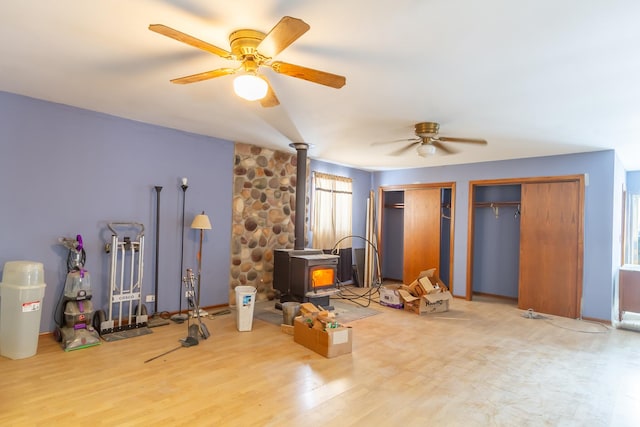 bedroom with a wood stove, ceiling fan, multiple closets, and wood finished floors