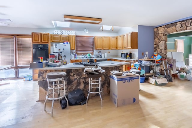 kitchen with a skylight, light countertops, freestanding refrigerator, light wood-type flooring, and black oven