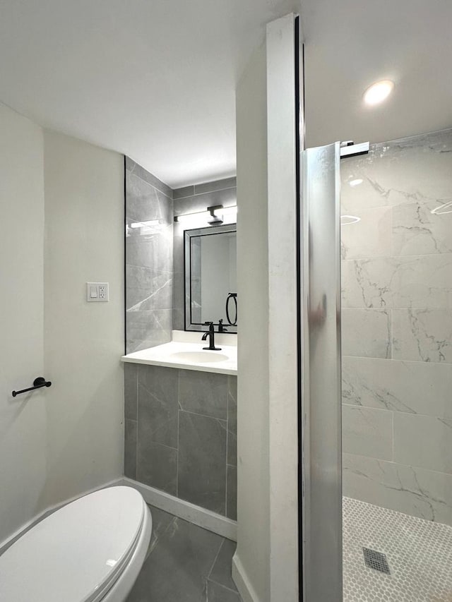 bathroom featuring sink, a tile shower, and toilet