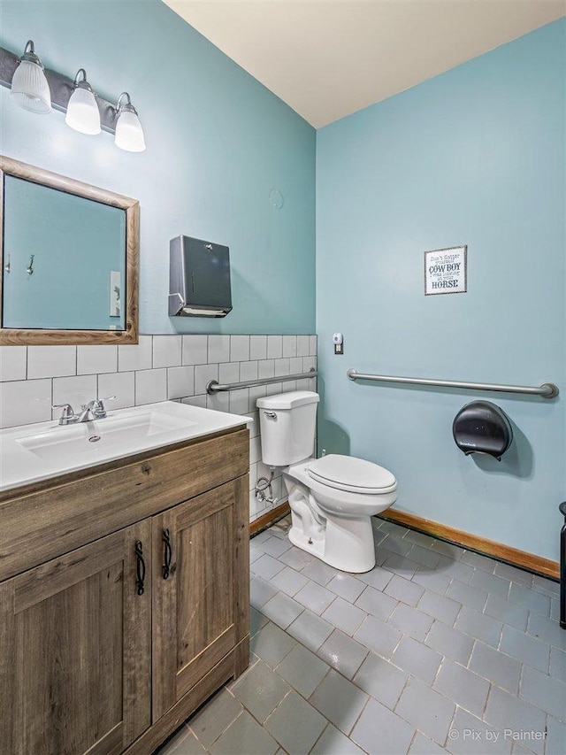 half bath featuring tile walls, toilet, wainscoting, vanity, and tile patterned flooring