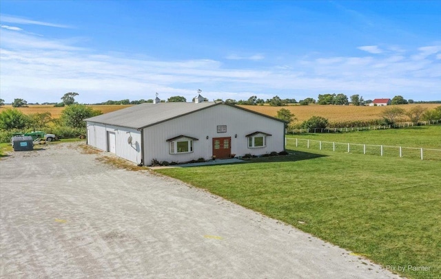 view of front of home featuring dirt driveway, fence, a garage, a rural view, and a front lawn