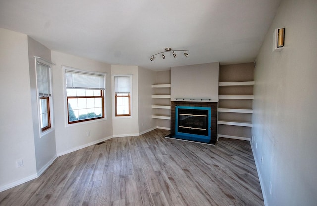 unfurnished living room with baseboards, a fireplace with flush hearth, built in features, and wood finished floors