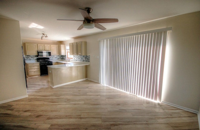 kitchen with light wood finished floors, stainless steel microwave, black gas range oven, a sink, and a peninsula