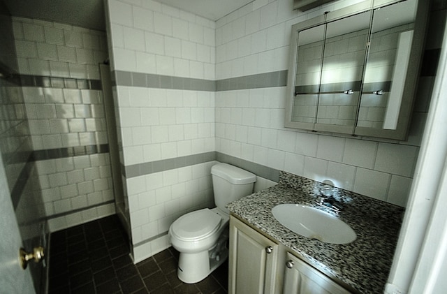 bathroom with toilet, vanity, tile patterned flooring, and tile walls