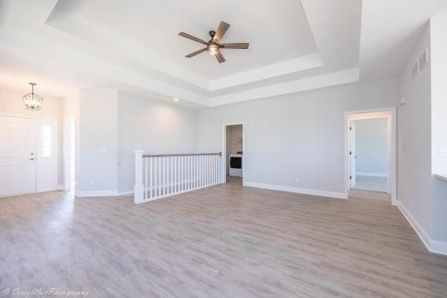 empty room featuring a raised ceiling, light hardwood / wood-style flooring, and ceiling fan with notable chandelier