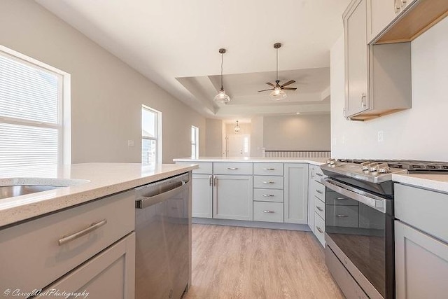 kitchen with ceiling fan, gray cabinets, a tray ceiling, light hardwood / wood-style floors, and stainless steel appliances