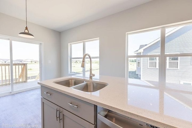 kitchen featuring light stone countertops, decorative light fixtures, stainless steel dishwasher, and sink