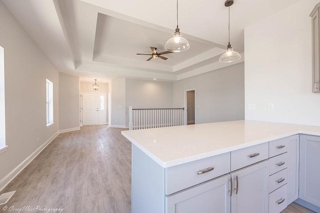 kitchen featuring pendant lighting, ceiling fan, a tray ceiling, light hardwood / wood-style floors, and kitchen peninsula