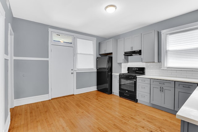 kitchen with gray cabinets, backsplash, light hardwood / wood-style floors, and black appliances