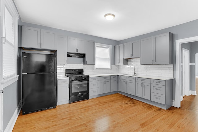 kitchen featuring tasteful backsplash, black appliances, gray cabinetry, sink, and light wood-type flooring