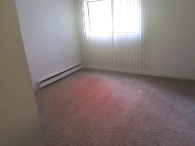 carpeted empty room featuring a baseboard heating unit